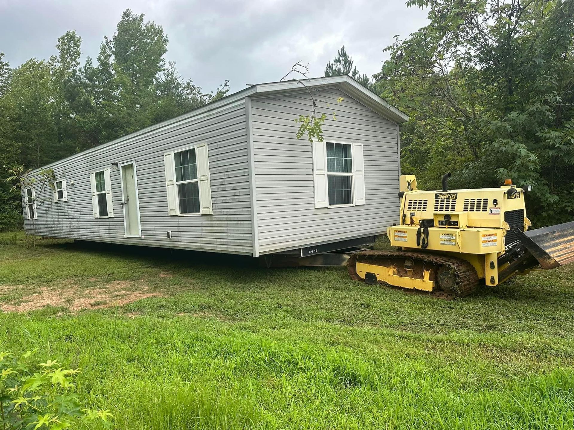 A mobile home is being moved by a bulldozer in a grassy field.