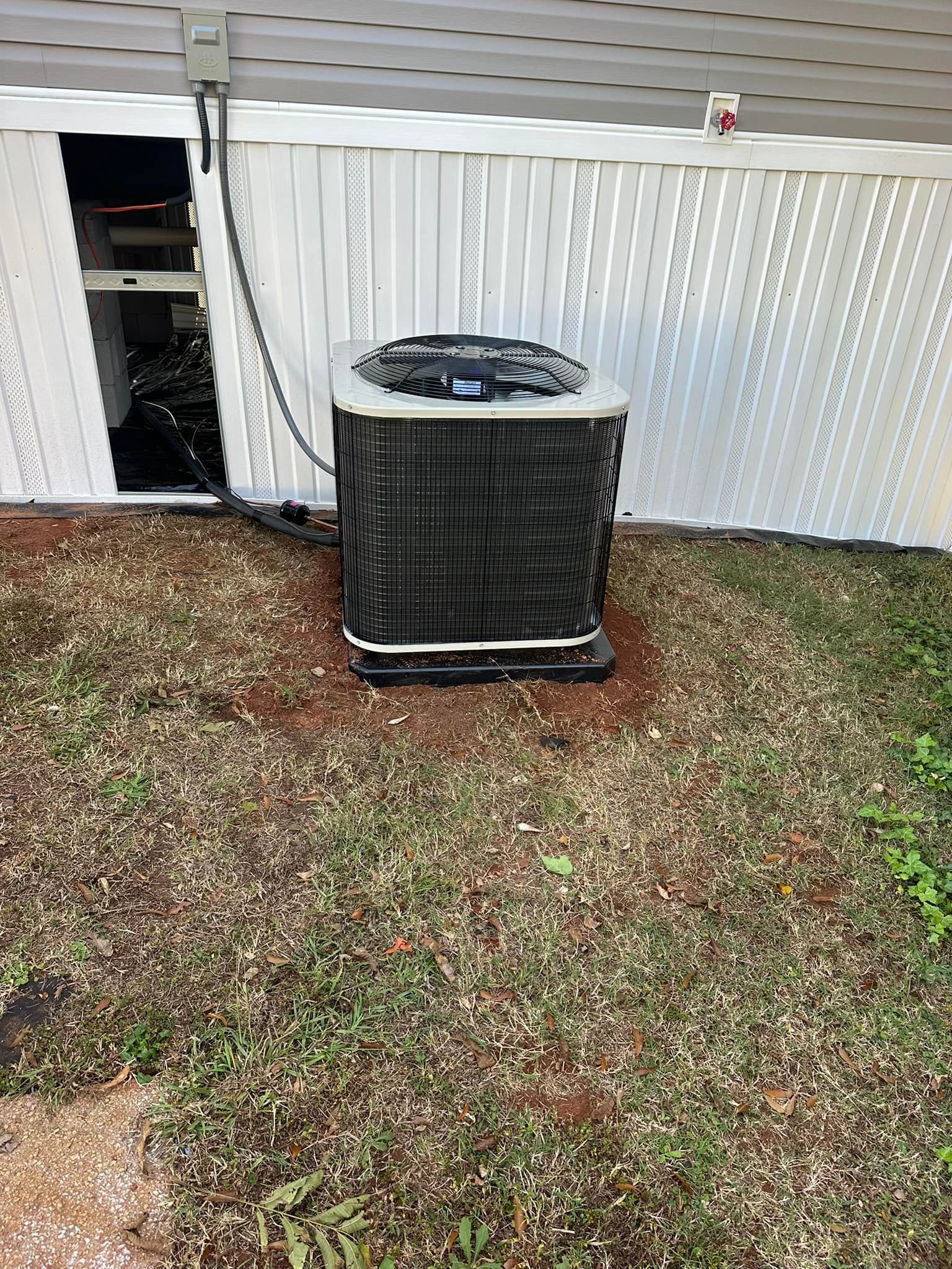 An air conditioner is sitting in the grass in front of a house.