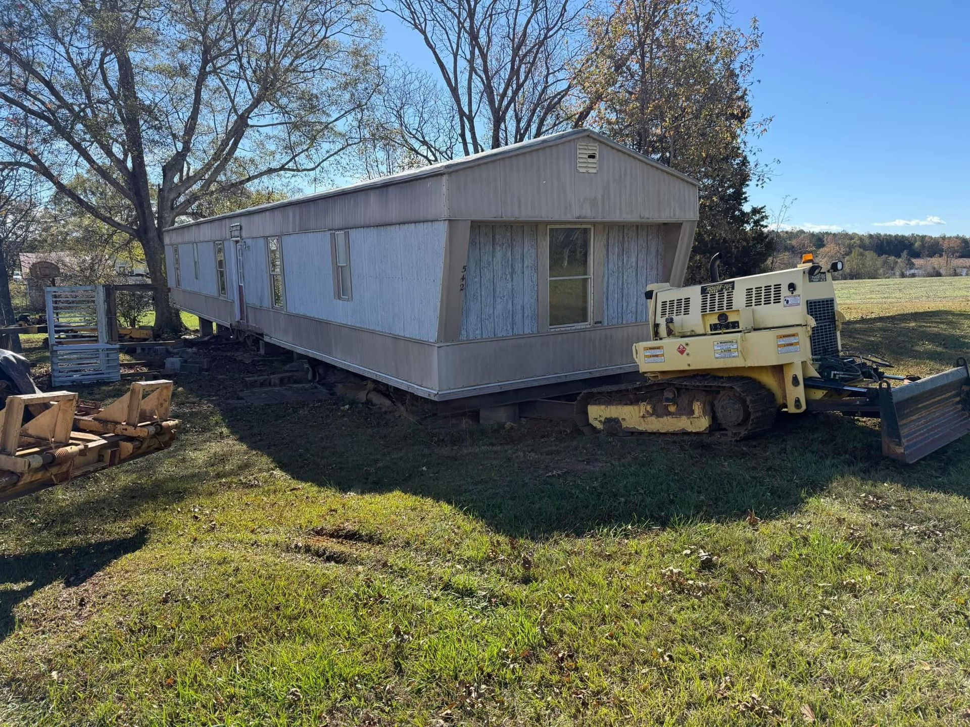 A mobile home is being moved by a bulldozer in a field.