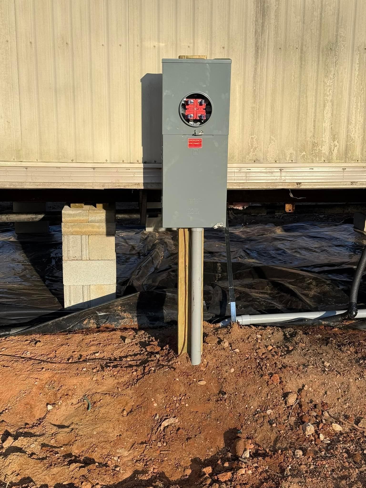 A electrical box is sitting in the dirt in front of a building.