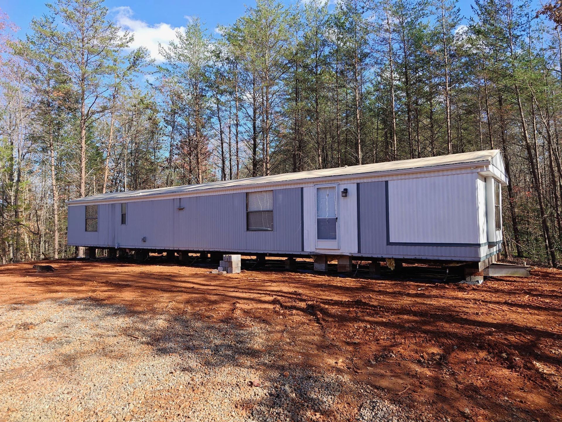 A mobile home is sitting in the middle of a dirt field surrounded by trees.