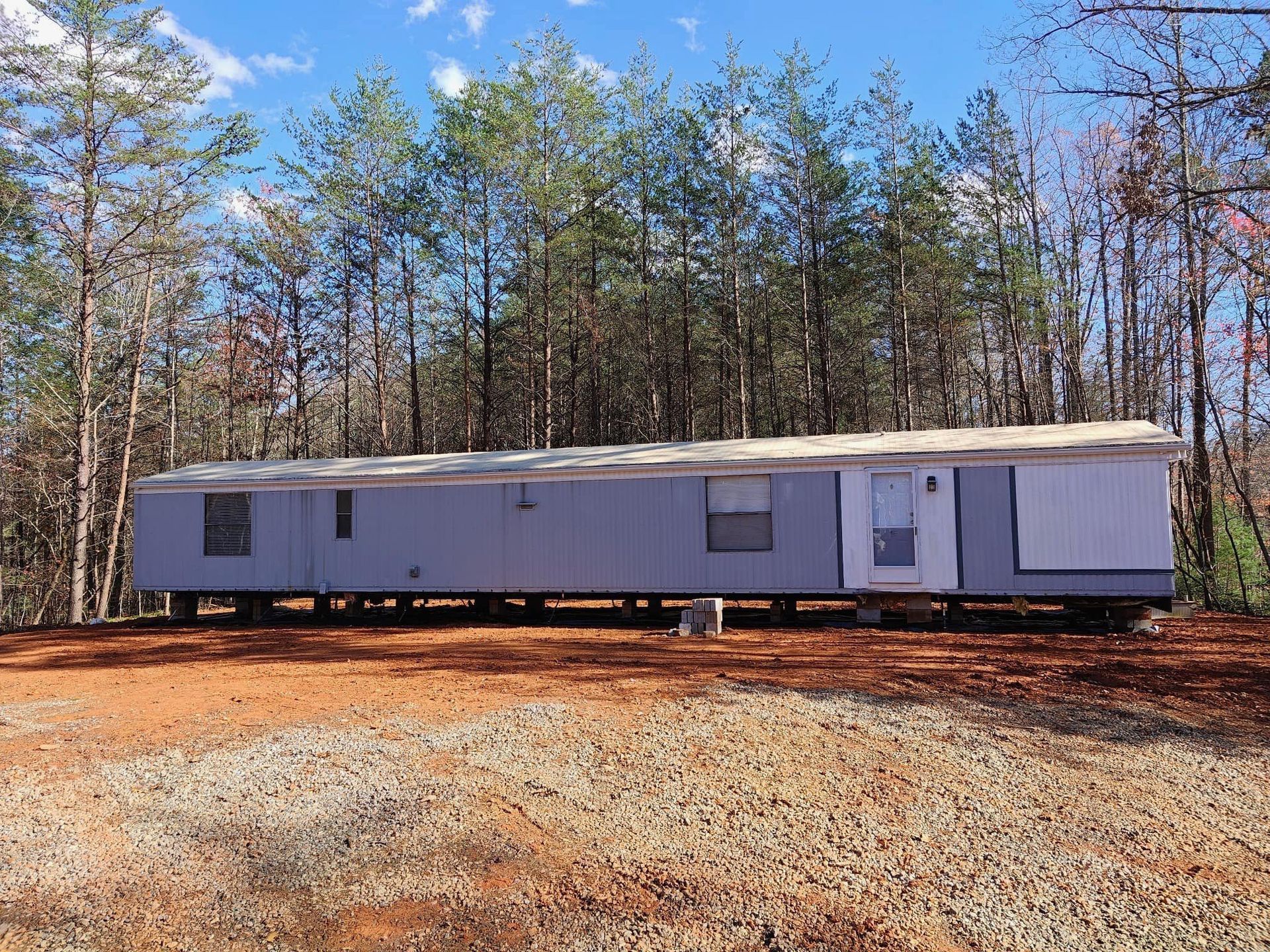 A mobile home is parked in a dirt field in the middle of a forest.