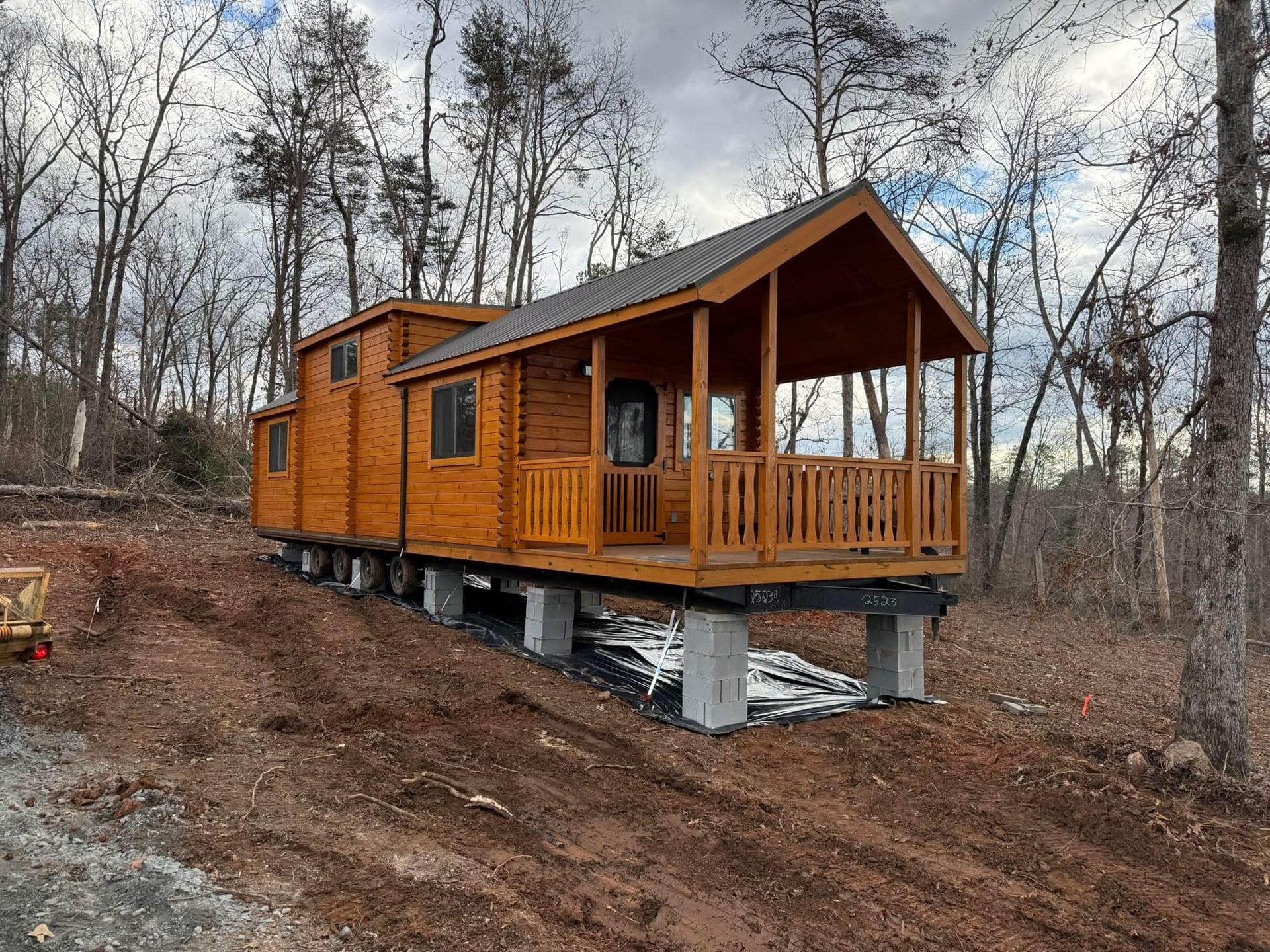 A small wooden house with a porch is sitting on top of a dirt field.