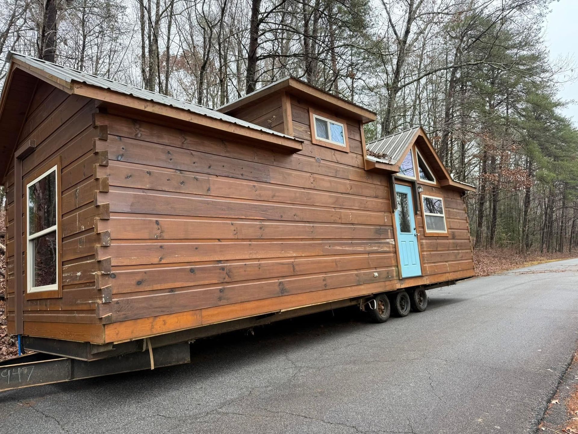 A small wooden house on a trailer is parked on the side of a road.