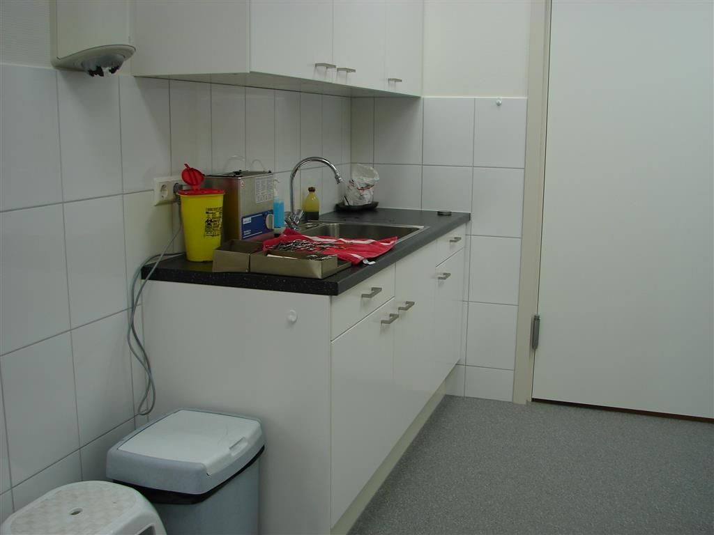 A kitchen with white cabinets a sink and a trash can