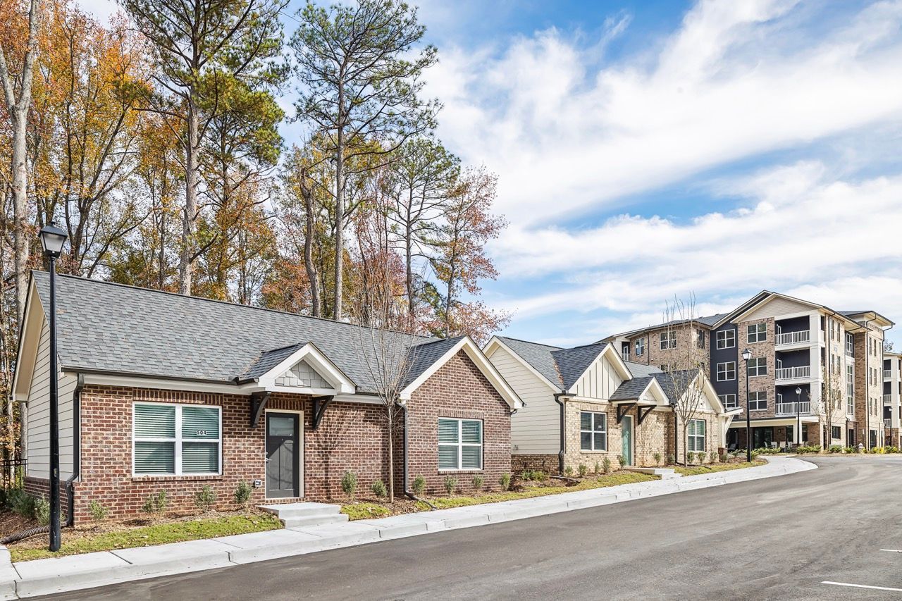 Row of brick-and-siding townhomes along a street with trees and blue sky