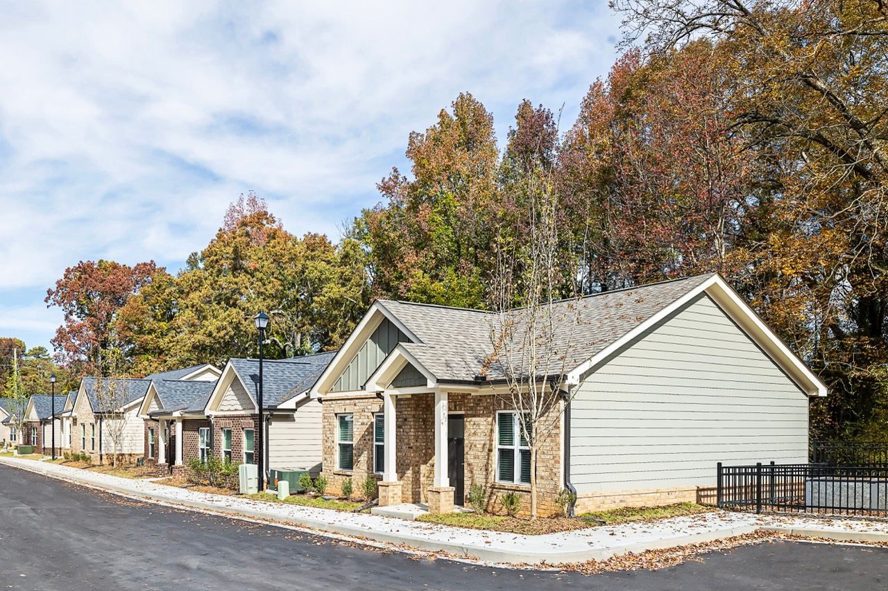 Row of single-story apartment buildings along a tree-lined street with autumn foliage.