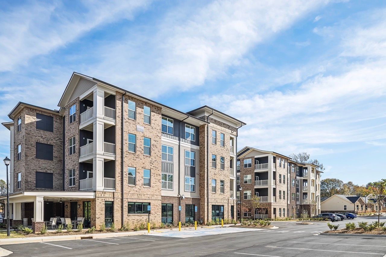 Exterior view of a multi-story brick apartment building with balconies and a parking lot.