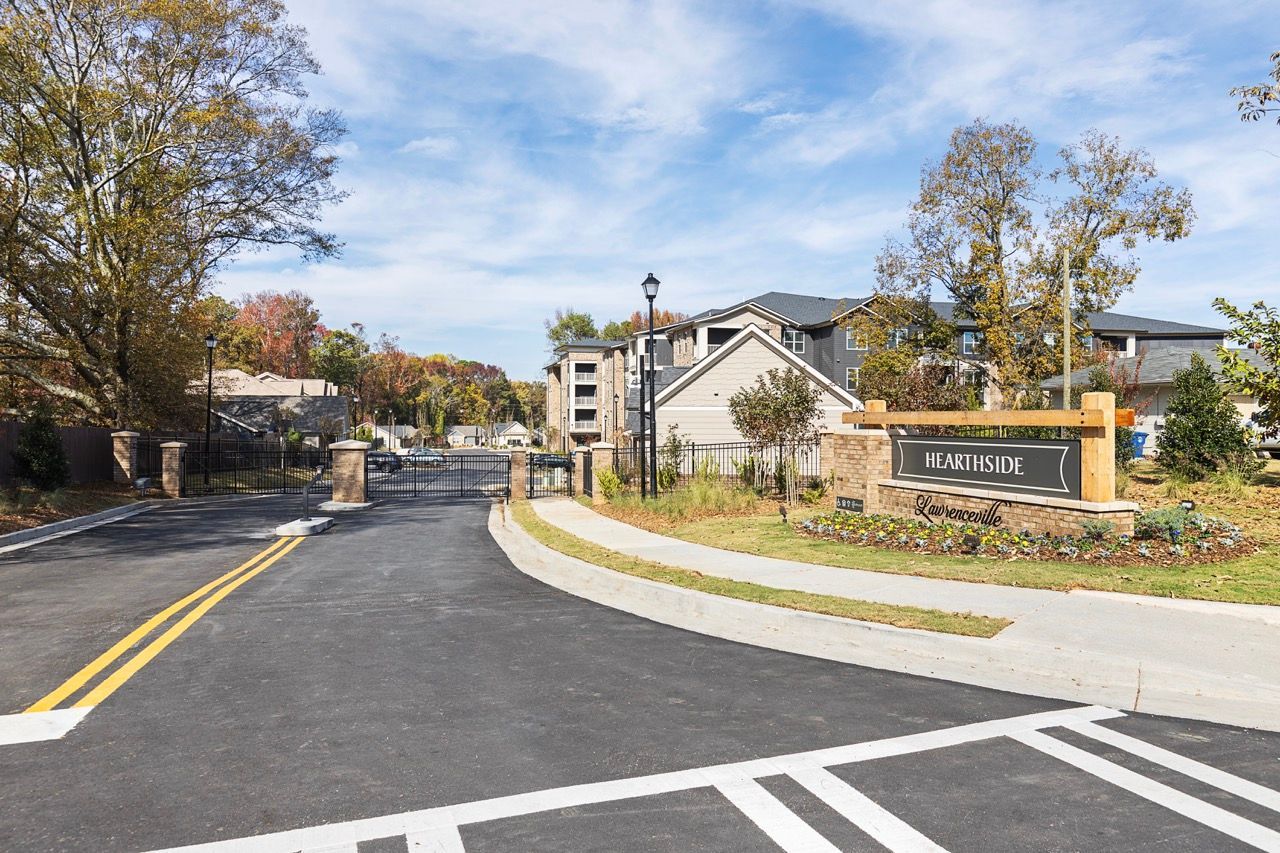 Gated apartment community entrance with a sign and landscaped surroundings.