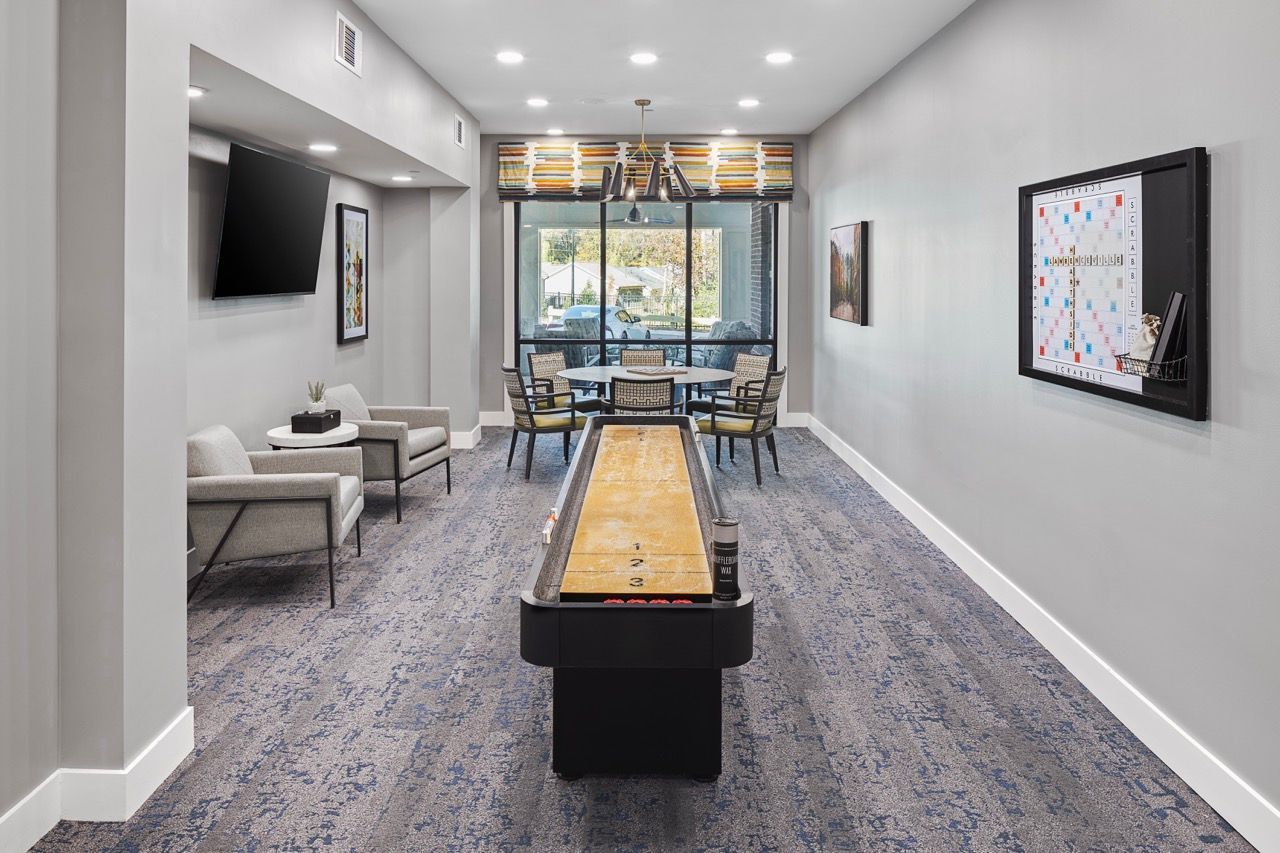 Common lounge with shuffleboard table, couches, wall art, and a large window.