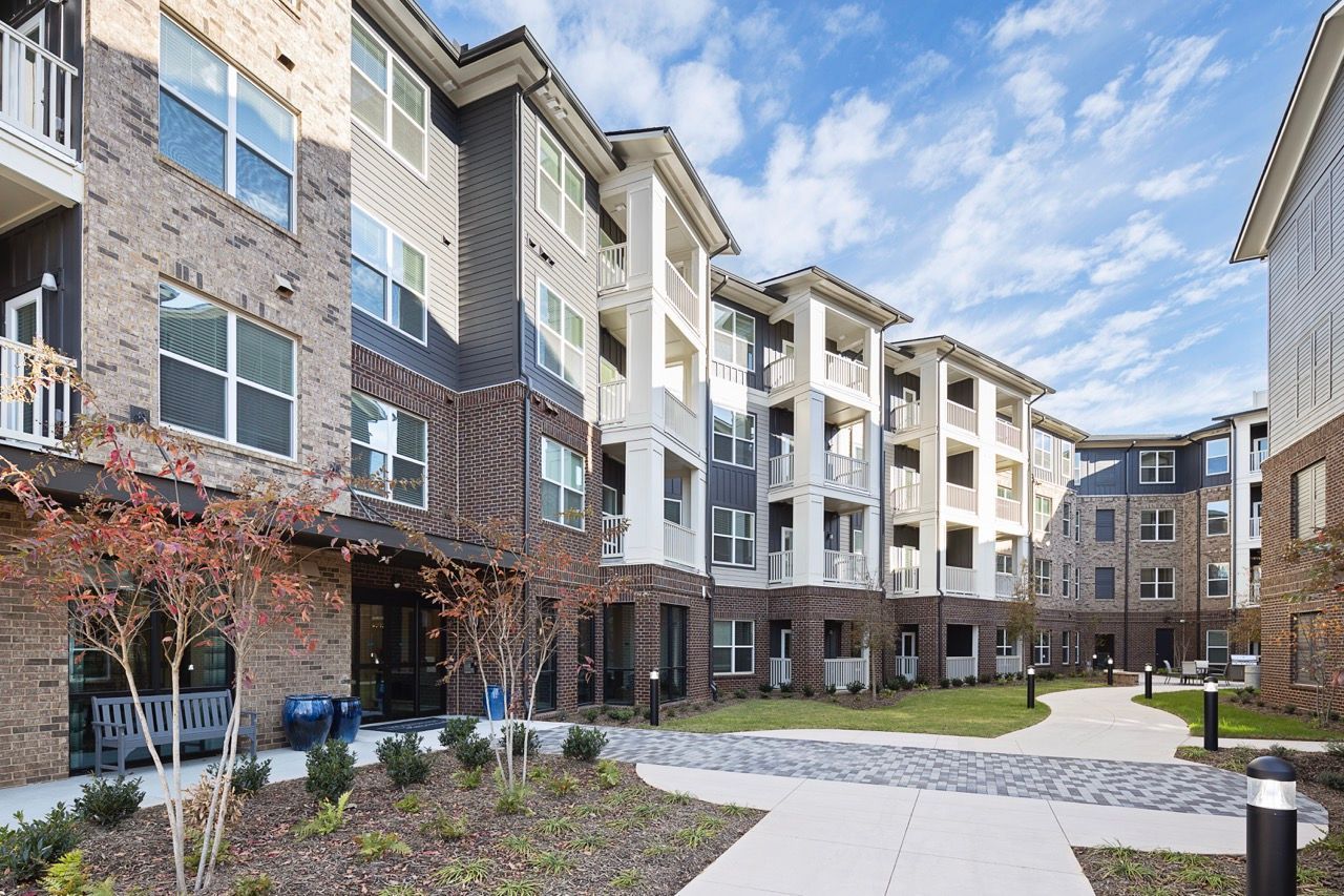 Exterior view of a modern apartment community with brick and siding buildings, balconies, and a landscaped courtyard.