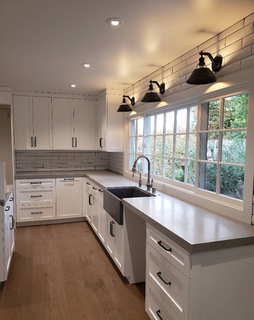 Bright white kitchen with long window, farmhouse sink, wood counters, and black pendant lights