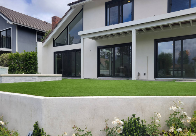 Modern white house with large glass doors, green lawn, and a low white retaining wall in front.