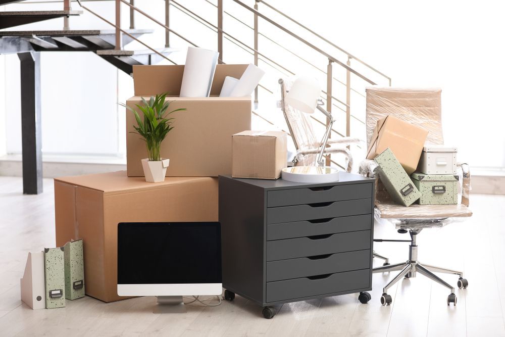 Office relocation: Boxes, desk, chair, monitor, plants, and supplies piled up near staircase.
