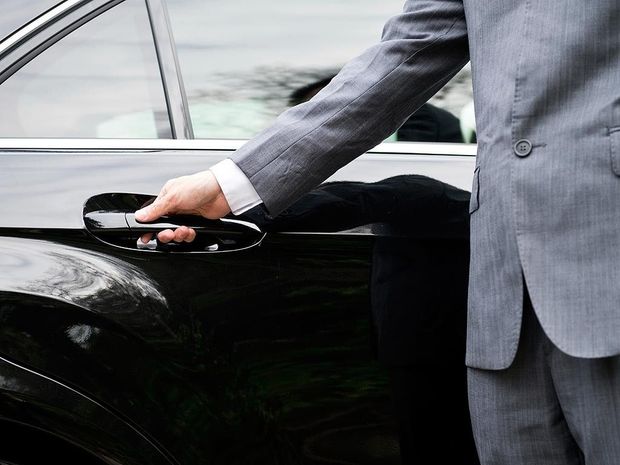 A man in a suit is opening the door of a black car.