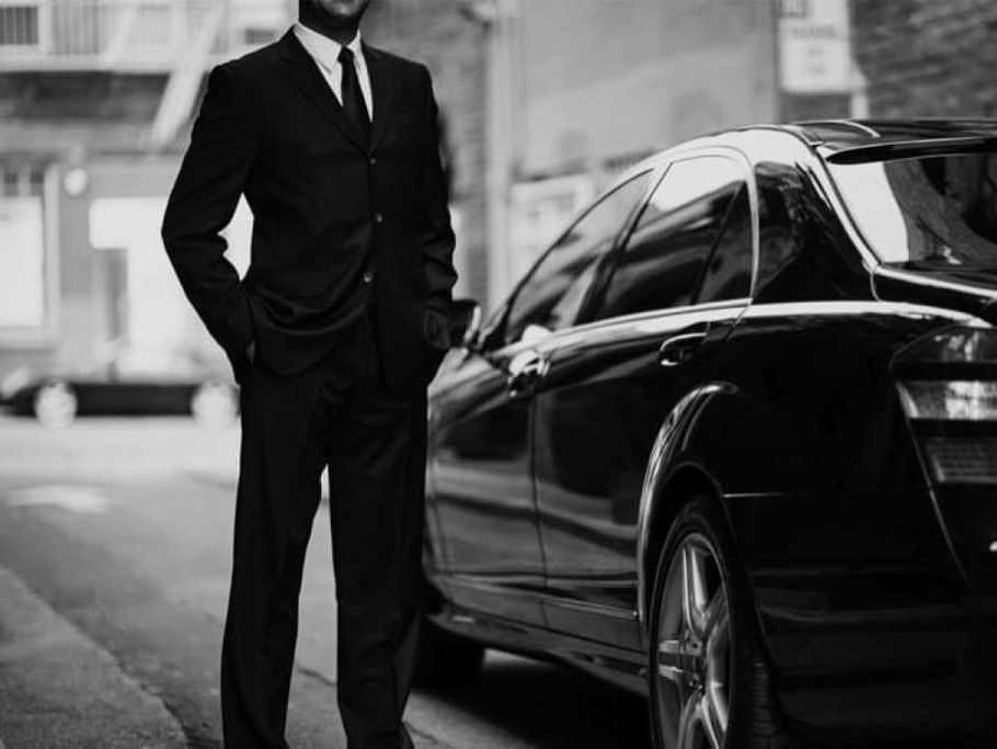 A man in a suit and tie is standing next to a black car.