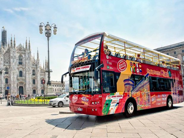 A red double decker bus is parked in front of a cathedral.