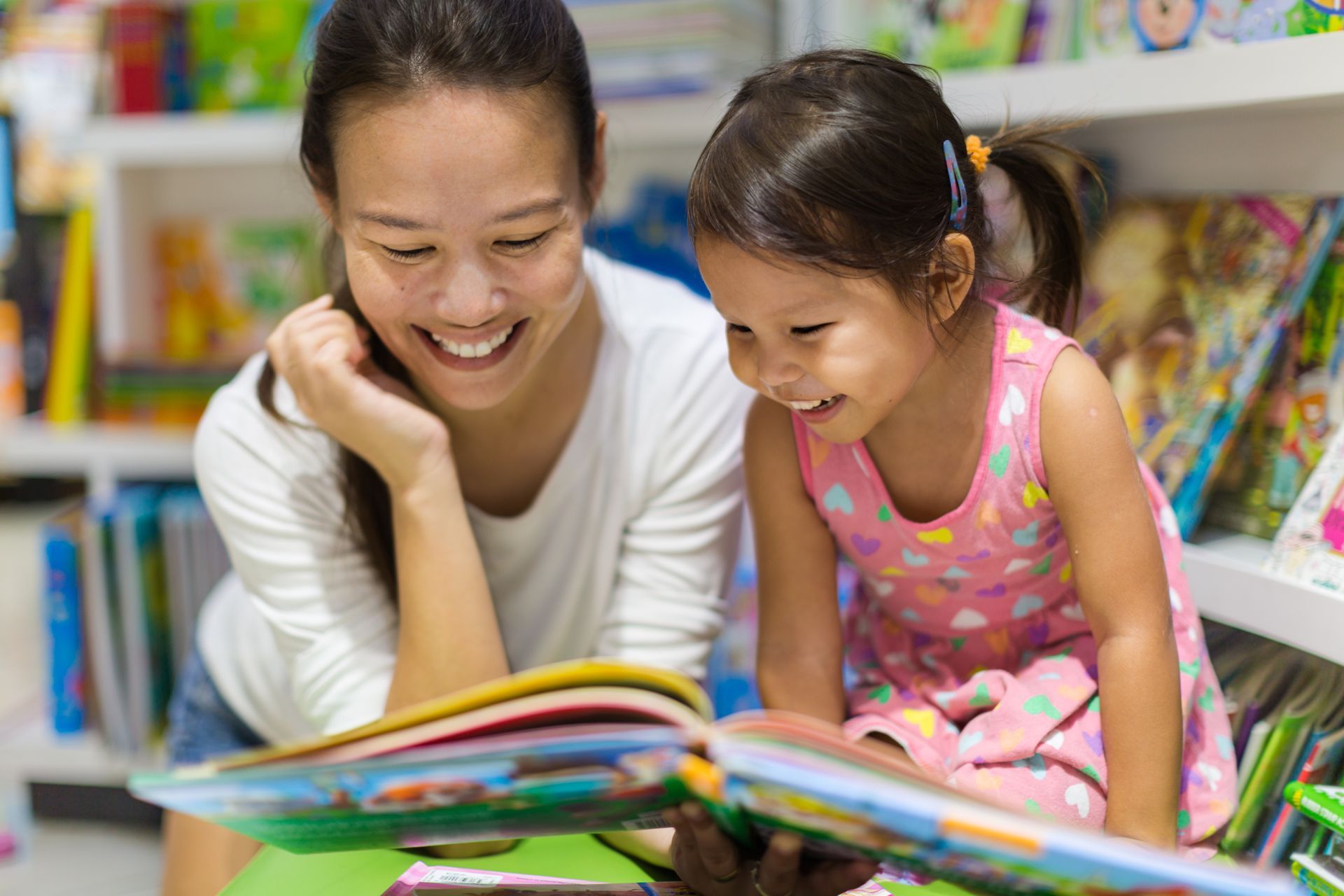 A woman is reading a book to a little girl in a library.