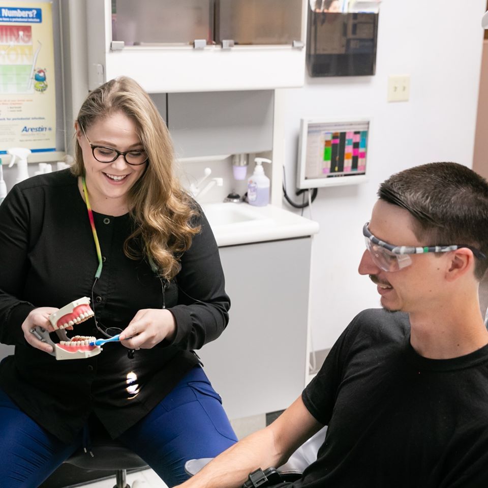 A woman is showing a man how to brush his teeth