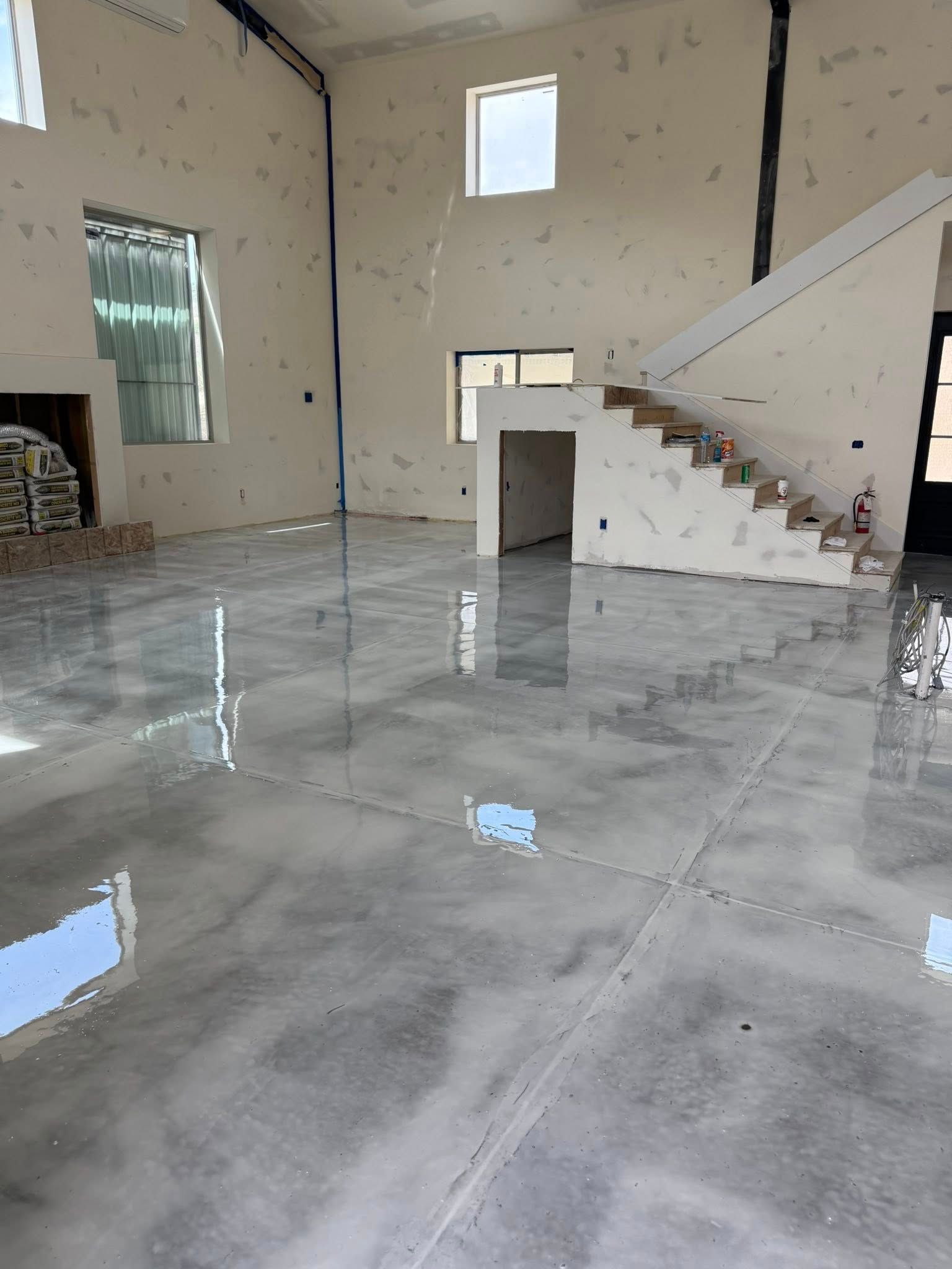 Large, open room with glossy, gray floor and exposed walls, staircase.