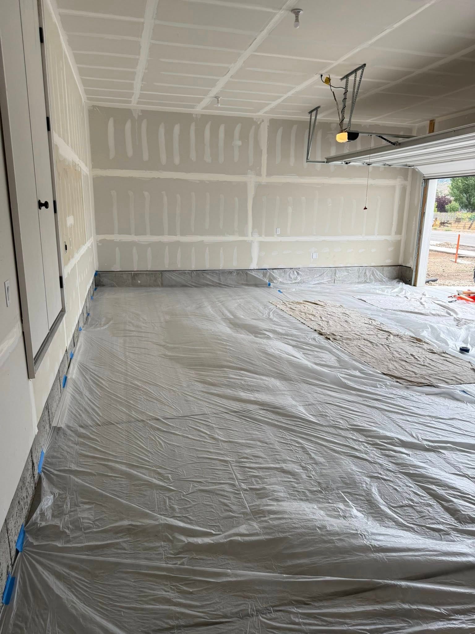 Garage interior with gray tarp covering the concrete floor; unfinished walls and ceiling.