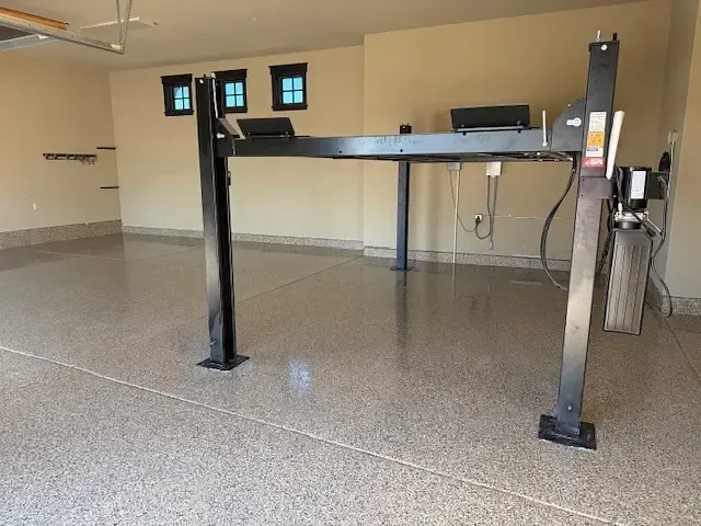 Black car lift in a spacious, epoxy-floored garage.