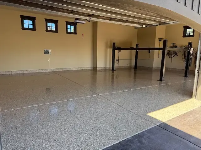 Spacious garage with epoxy flooring and car lift, beige walls, sunlight streaming in.