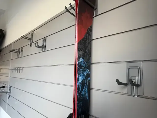 A ski with red and black design mounted on a white wall with hooks.