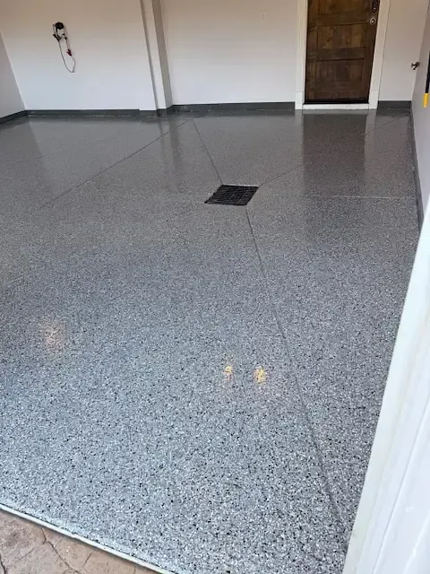 Gray speckled epoxy garage floor, with drain in the center and white walls.