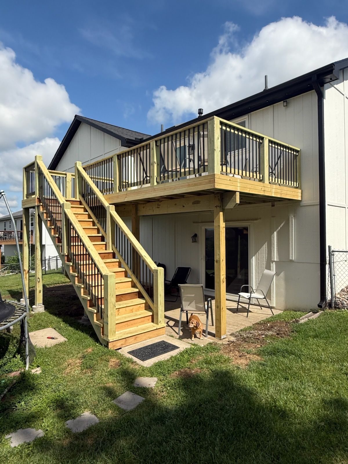 A wooden deck with stairs leading up to it is in the backyard of a house.
