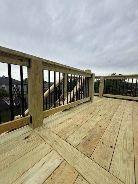 A wooden deck with a metal railing and a cloudy sky in the background