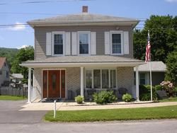 Two-story beige house with white trim and a covered porch, displaying an American flag.