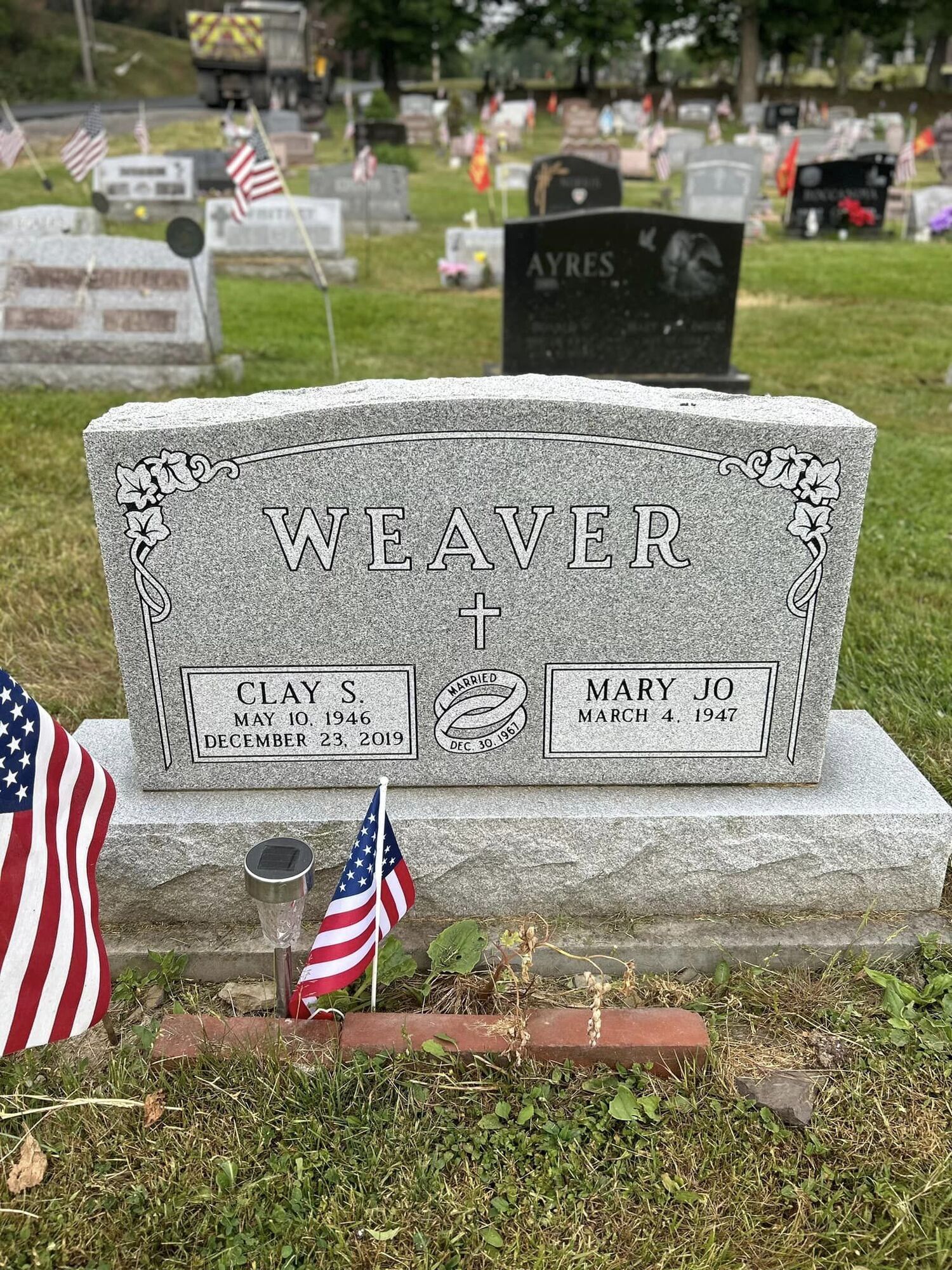 Gravestone of Clay and Mary Weaver in a cemetery, marked with American flags.