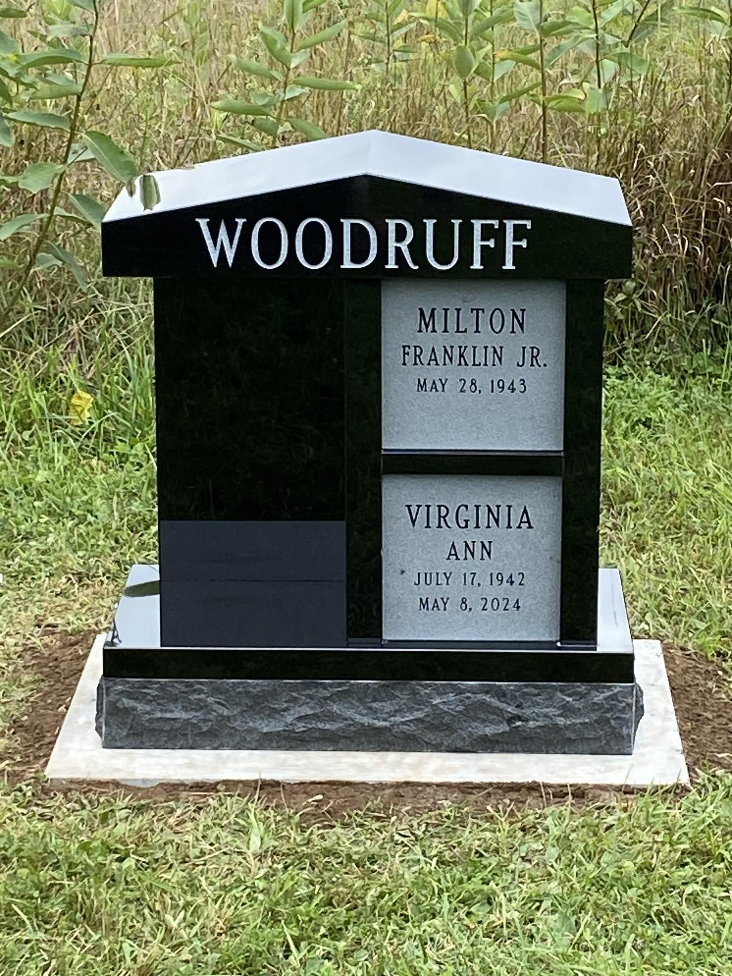 Black granite Woodruff headstone with names, dates, and dark gray base, set in grass.