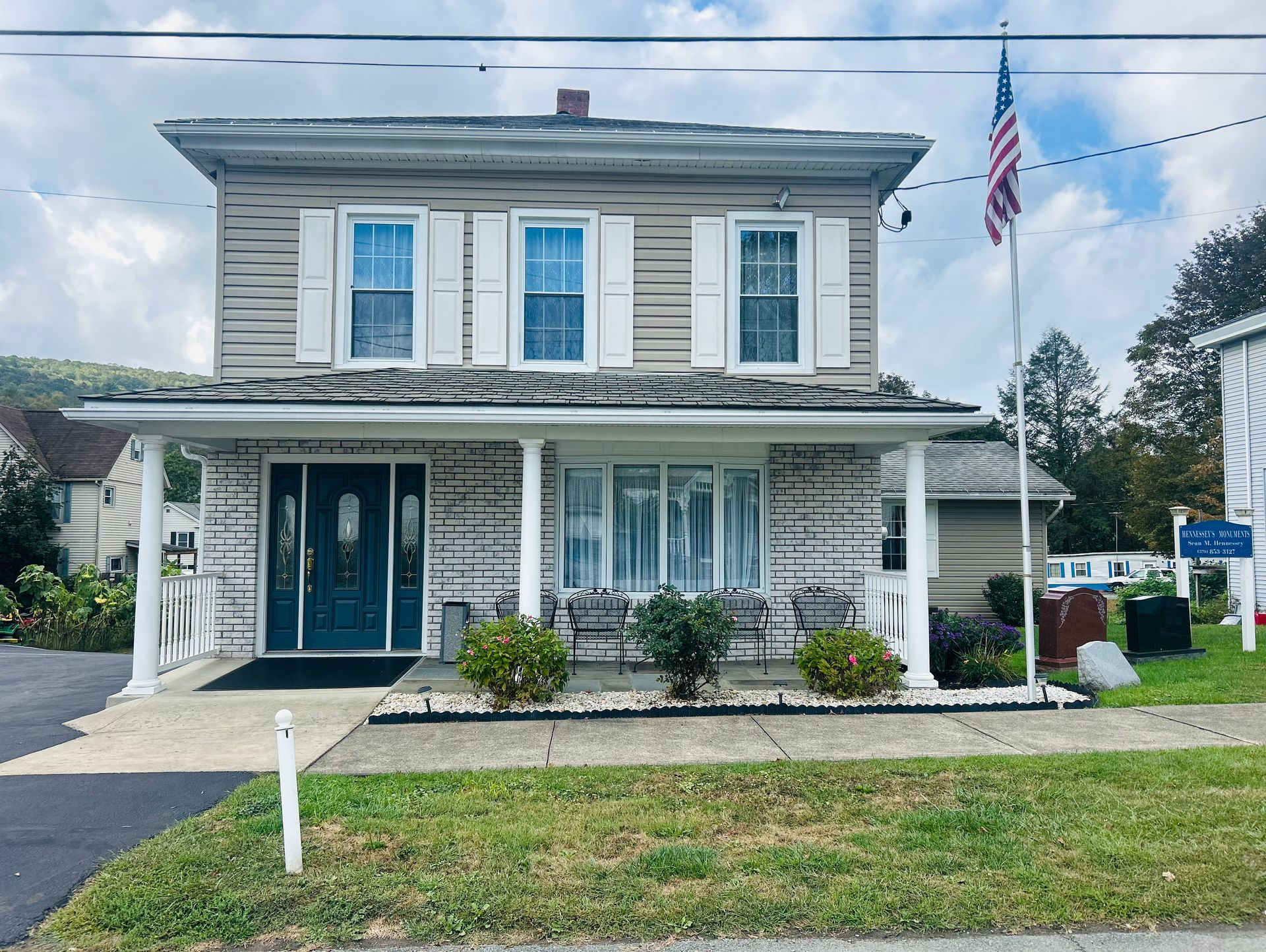 Two-story beige house with white trim and a covered porch, displaying an American flag.