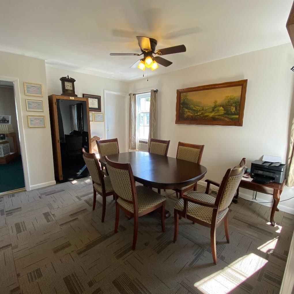 Dining room with oval table, chairs, artwork, and cabinet.