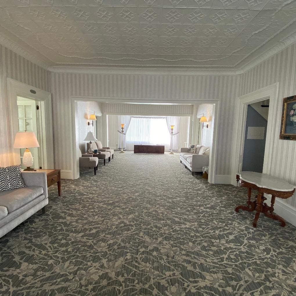 Elegant waiting room, grey floral carpet, two sofas, chairs, lamps, and doorway with natural light.