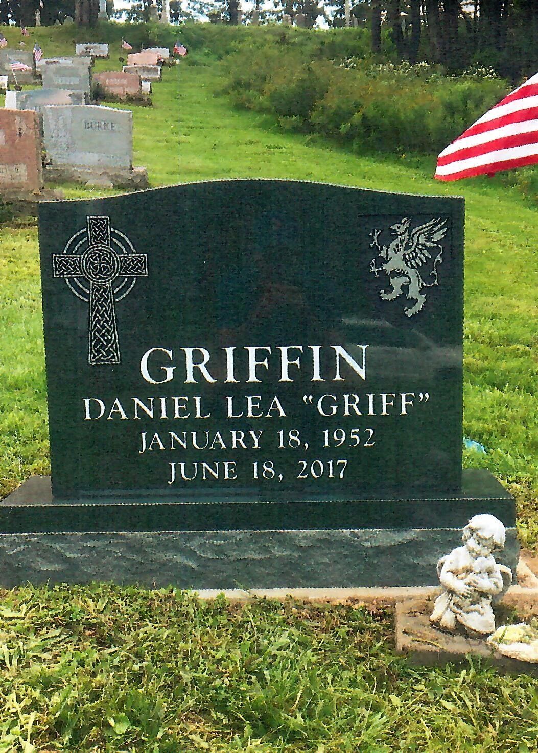 Green granite tombstone with Celtic cross and lion, GRIFFIN inscription, dates 1952-2017, and American flag in background.