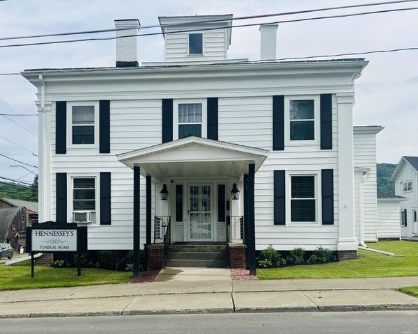 White two-story building with black shutters, a small porch, and a sign on the lawn.