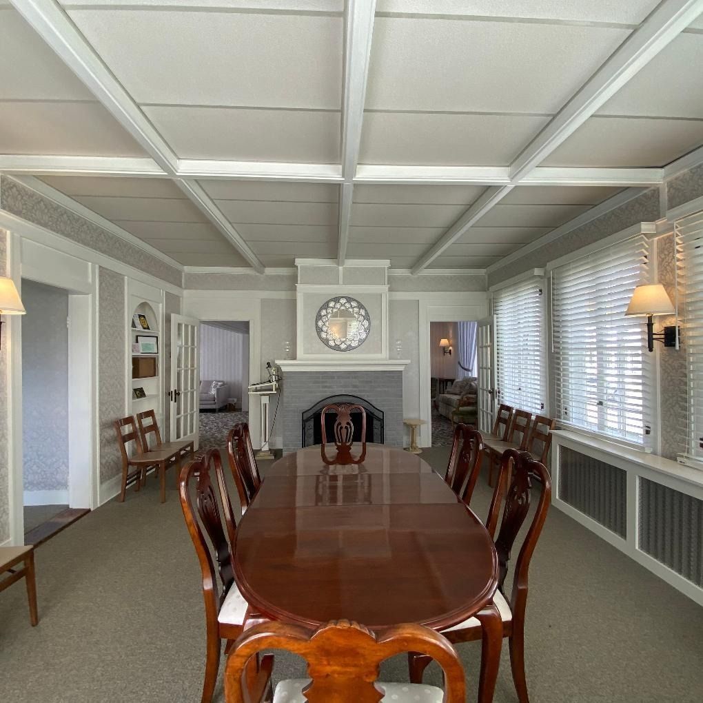 Formal dining room with a long wood table and chairs. Fireplace, neutral walls, windows.