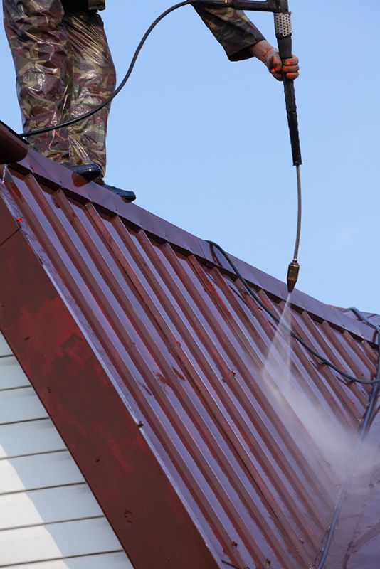 Person Pressure-washing a Red Metal Roof With Water Spray — A1 Roof Cleaning In Childers, QLD