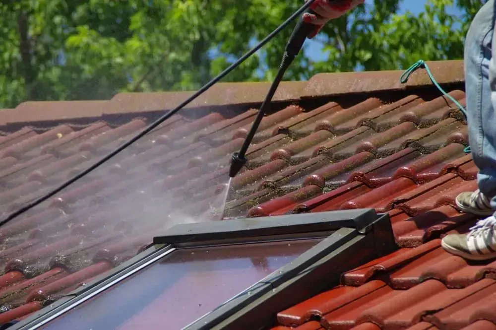 A Person Uses a Pressure Washer to Clean Red Roof Tiles — A1 Roof Cleaning In Kepnock, QLD