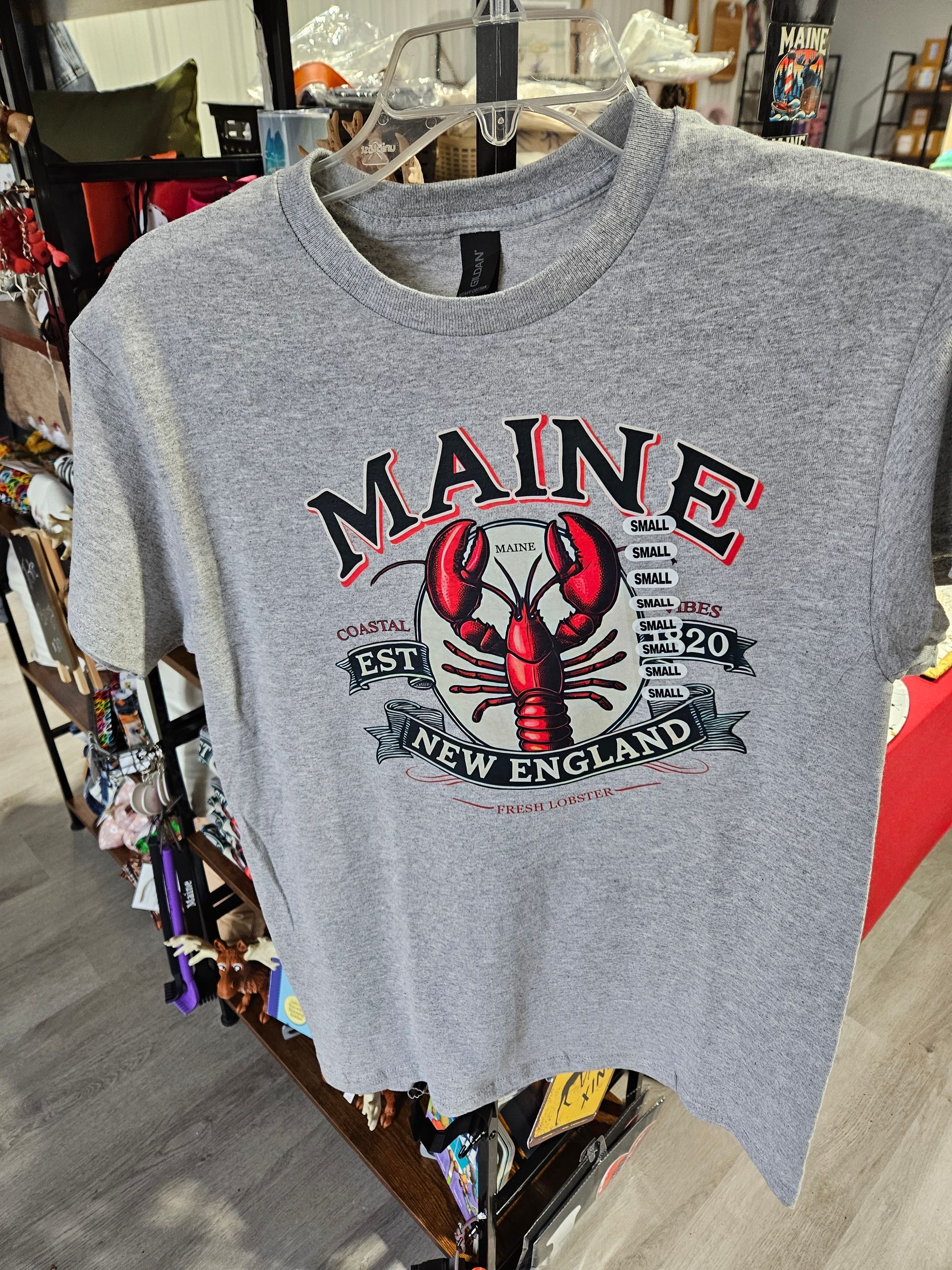 A gray maine lobster t-shirt is hanging on a rack in a store.