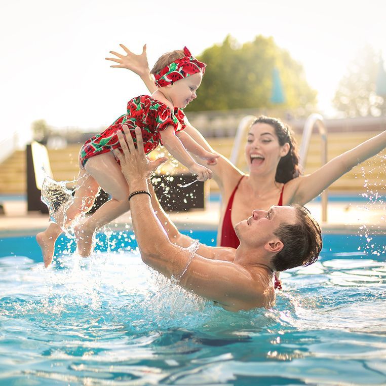 Un homme tient un bébé en l’air dans une piscine.