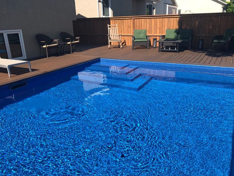 Une grande piscine bleue avec une terrasse en bois et des chaises autour.