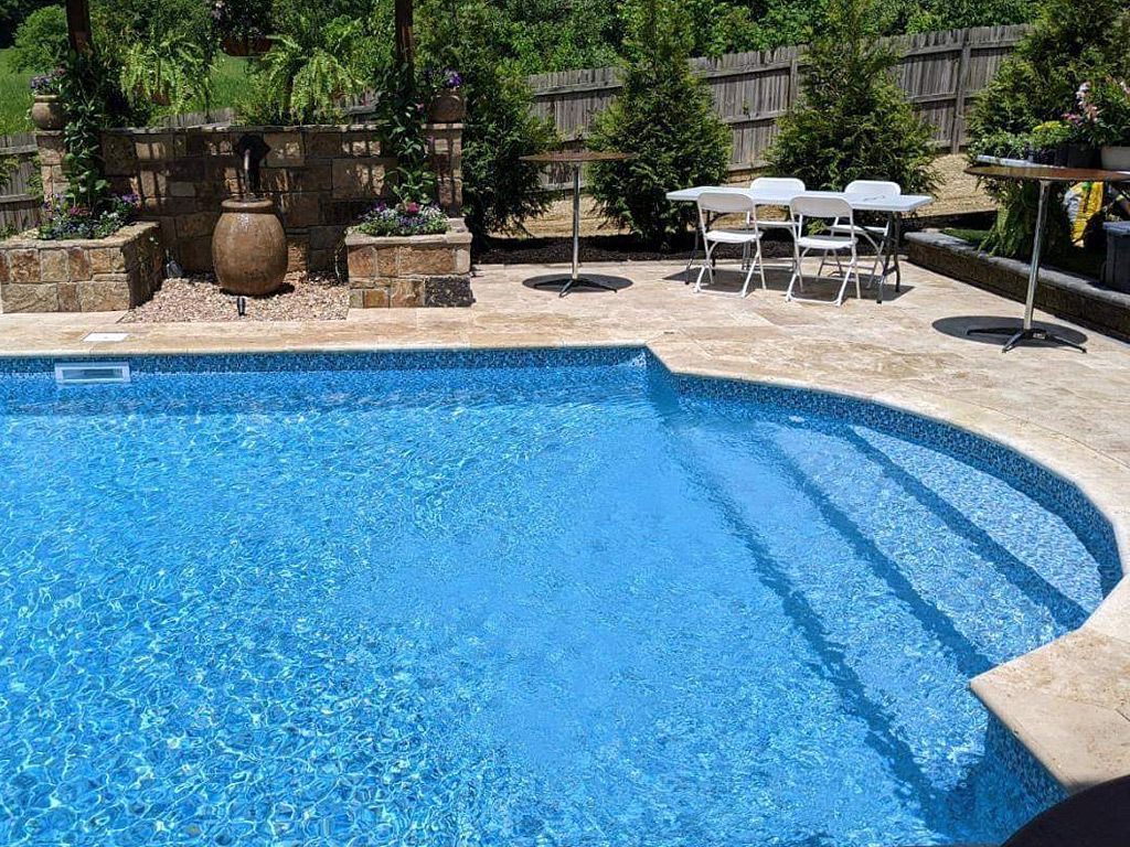 Une grande piscine avec des escaliers qui y mènent et une table et des chaises en arrière-plan.