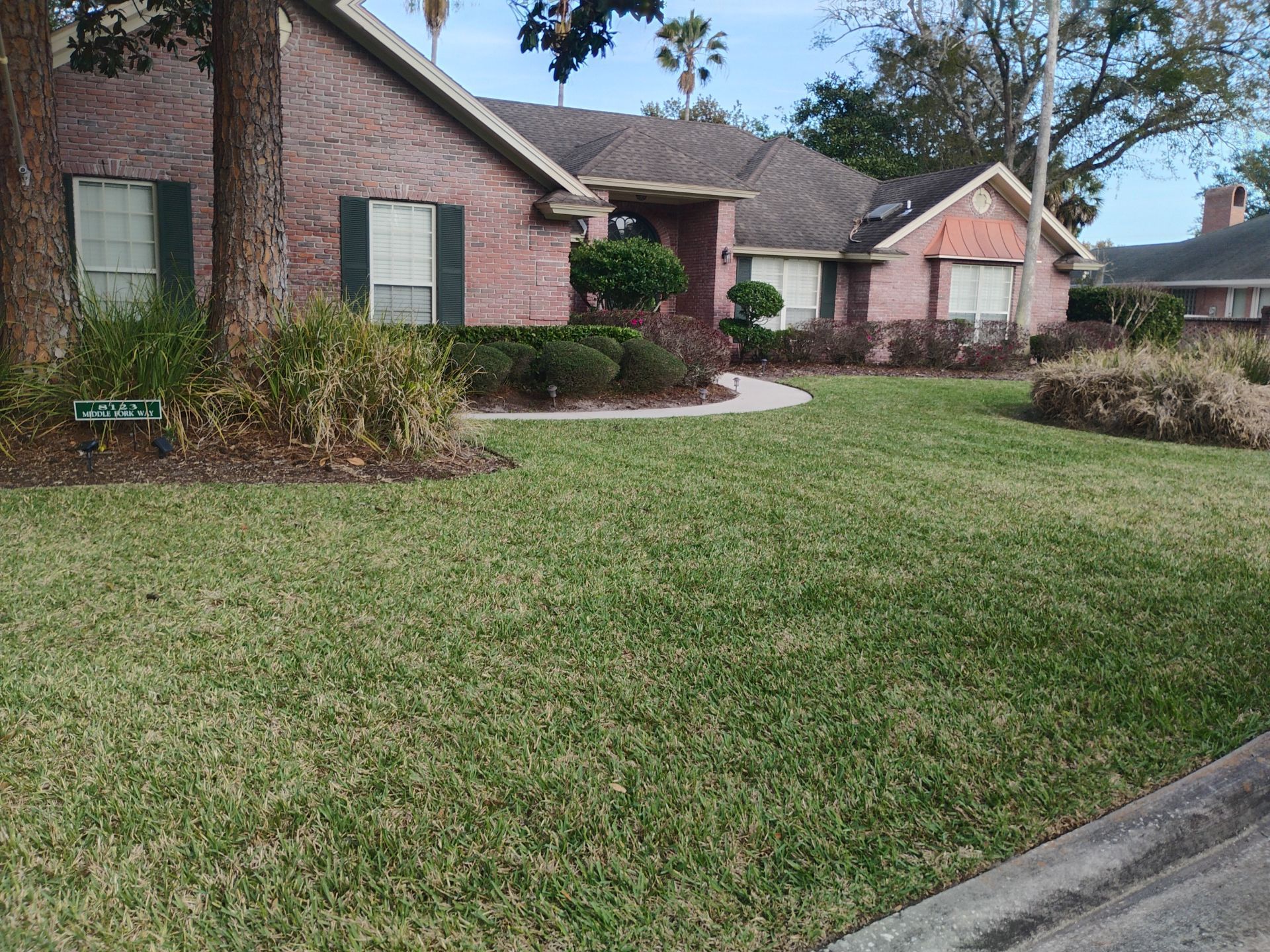 Suburban brick house with green lawn, shrubs, and a sidewalk in front