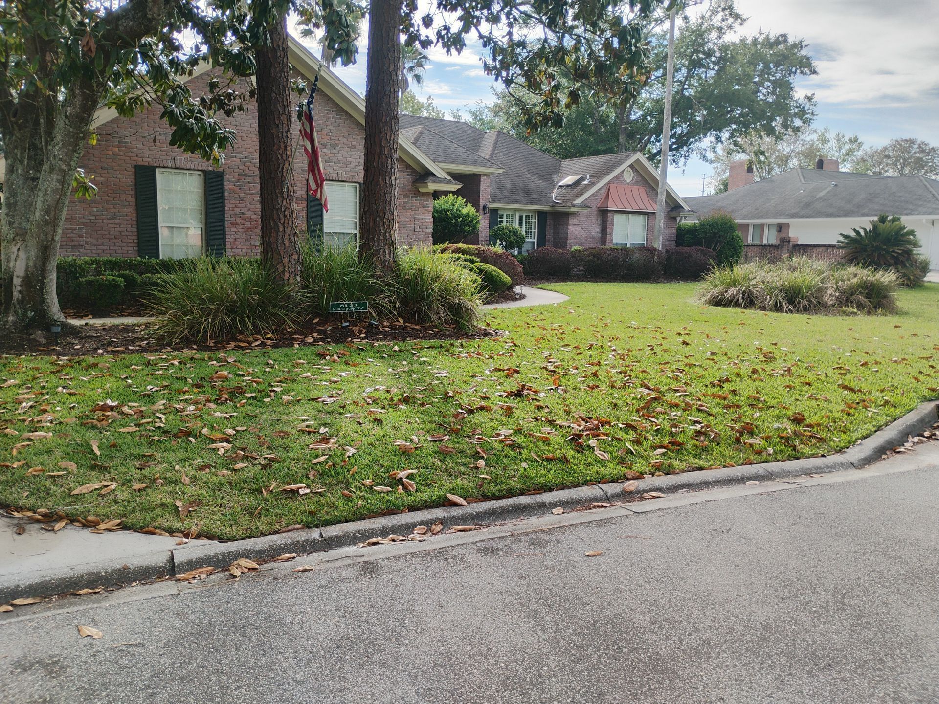 Brick suburban house with green lawn, trees, and a curved driveway on a quiet street.