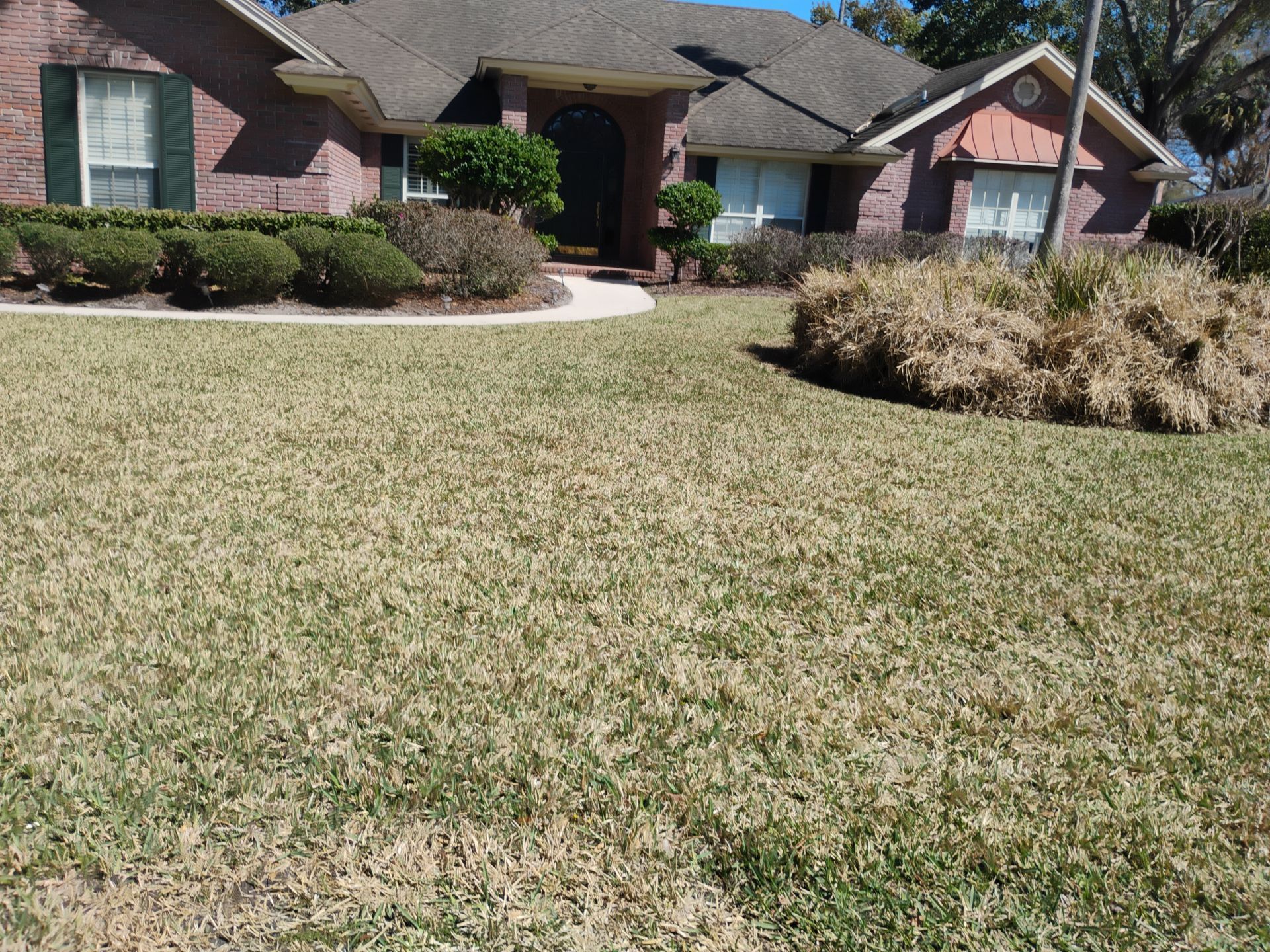Suburban brick house with a front lawn, curved walkway, and shrubs in daylight