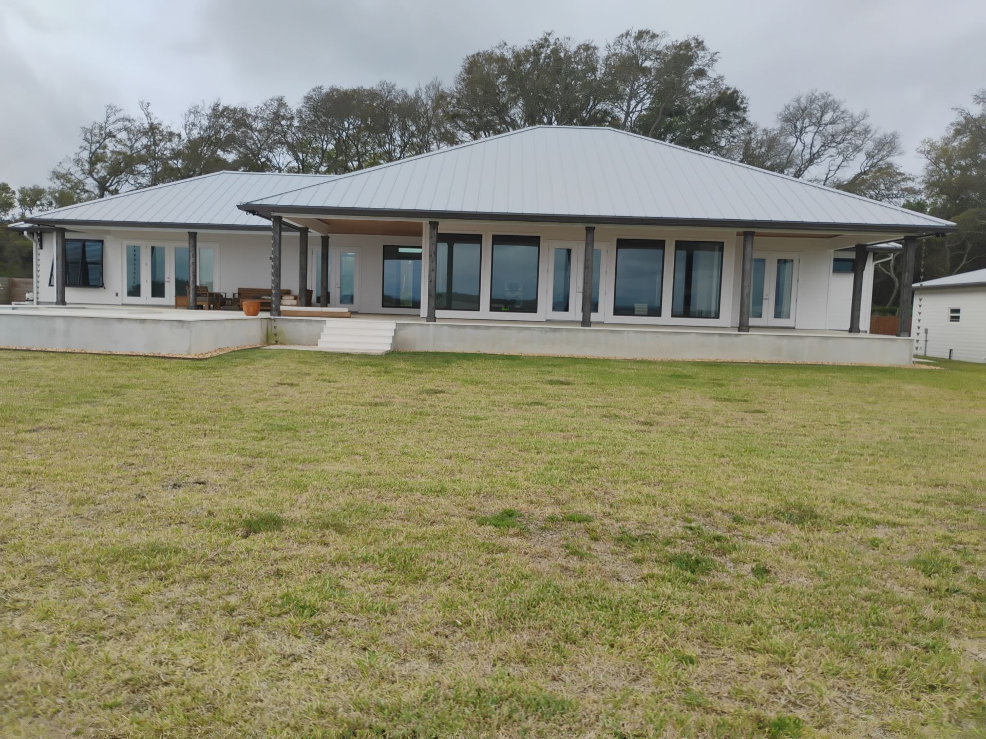 Single-story white house with a metal roof and large front windows, set behind a grassy lawn.